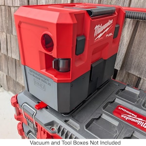 Puede incluir: Un organizador de herramientas Milwaukee Fuel Packout rojo y gris con un asa roja. El organizador tiene una sección superior roja con una abertura circular y una base gris. El logotipo de Milwaukee es visible en el lateral. El texto "Vacuum and Tool Boxes Not Included" está en la parte inferior.