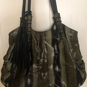 May include: An olive green and black handbag with a textured pattern and black leather handles. The bag has a decorative black tassel and a gathered design. The bag is designed with a shoulder strap.