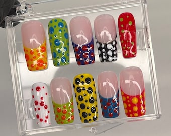 Peut inclure: Un ensemble de dix faux ongles avec une pointe blanche et un motif de pois de différentes couleurs, notamment rouge, jaune, bleu, vert et noir.