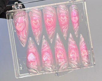 May include: A clear plastic box containing ten pink and white swirl-patterned fake nails with a heart design. The nails are arranged in two rows of five.