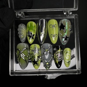 May include: A set of 10 green and black nail tips with various designs, including stars, bows, and swirls. The tips are displayed in a clear plastic case.