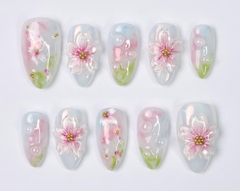 May include: Set of ten false nails with a white base and pink and white floral designs. Each nail has a pearl-like accent and gold glitter.
