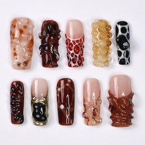 May include: Ten different nail designs featuring various textures and colors, including brown, red, white, and black. The designs include swirls, dots, and bubbles.