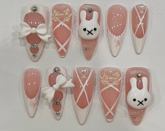 May include: Ten pink and white ballerina-themed nail tips with various designs, including bows, cross-hatching, and bunny faces.
