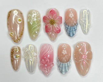 Puede incluir: Conjunto de diez uñas postizas con varios diseños. Las uñas son de forma ovalada y presentan una variedad de colores y patrones, incluyendo rosa, verde, blanco, azul y dorado. Algunas uñas tienen flores, lazos y otros elementos decorativos.