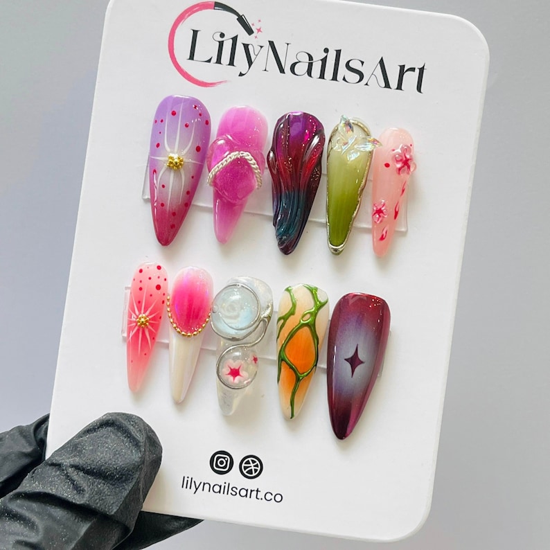 May include: A display of ten different nail art designs. The designs feature various colors, patterns, and embellishments, including flowers, glitter, and rhinestones. The designs are displayed on a white background with the text "LilyNailsArt" and "lilynailsart.co" at the top and bottom.