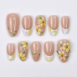 May include: Set of ten false nails with a nude base and white tips. Some nails have yellow and green floral designs.