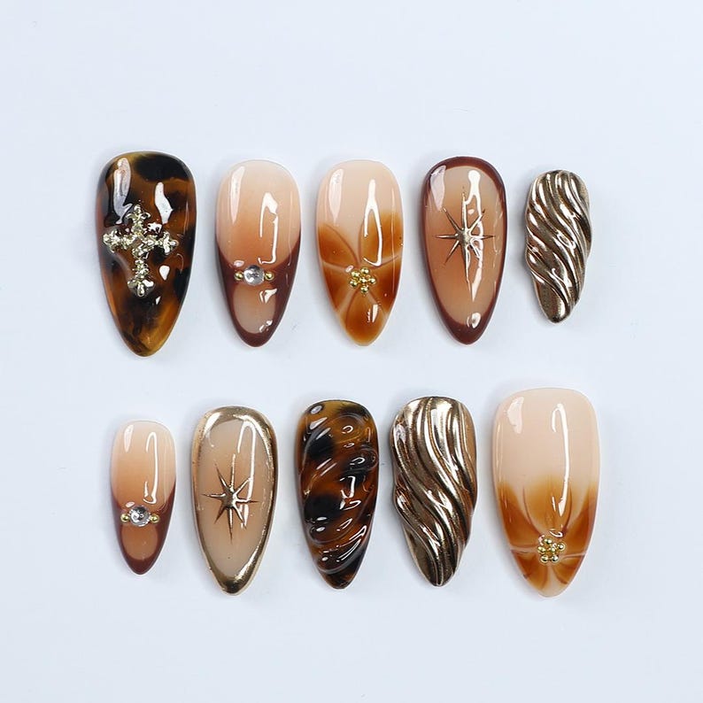 Uñas postizas de otoño con detalles en carey y dorado 3D, uñas en marrón almendra medio y nude con diseño de estrella y cromo texturizado.