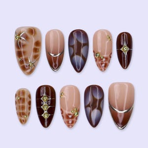 May include: A set of ten almond-shaped press-on nails featuring a color palette of nude, brown, and deep chocolate. The designs include glossy finishes, metallic silver line accents, and small gold-toned spherical studs arranged in various patterns.
