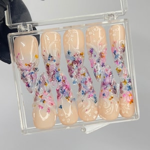Può includere: Set di sei unghie finte color nude con un design floreale. Le unghie sono decorate con piccoli fiori colorati e hanno una finitura trasparente e lucida.