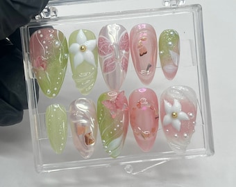 May include: A set of ten false nails with various designs. The nails are in a clear plastic case. The designs include butterflies, flowers, and swirls. The nails are in shades of pink, green, and white.