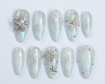 Puede incluir: Conjunto de diez uñas postizas blancas y azul claro con un diseño de copo de nieve y purpurina plateada. Algunas uñas tienen un adorno de copo de nieve plateado.