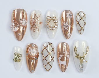 May include: Ten false fingernails with a variety of Christmas-themed designs. The designs include snowflakes, reindeer, a wreath, a bell, and a grid pattern. The nails are painted in a metallic gold color.
