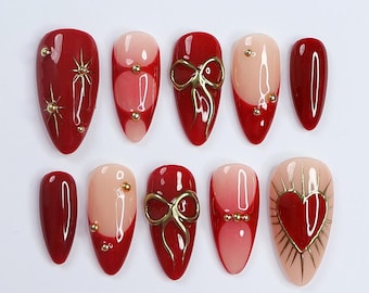 May include: Set of ten red and nude false nails with gold accents. Some nails feature a gold bow, others have gold stars, and one has a gold heart.