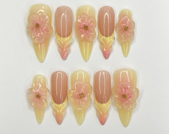 May include: Ten pale yellow and pink artificial nails with a 3D flower design. Each nail has a small gold accent in the center of the flower.