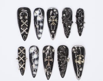 Könnte beinhalten: Zehn schwarze und silberne Nagelspitzen mit verschiedenen Designs. Die Designs umfassen Kreuze, Fleur-de-lis, Spikes und ein Spitzenmuster.