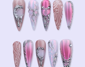 Puede incluir: Un conjunto de diez uñas artificiales con diversos diseños. Las uñas presentan un acabado brillante en tonos rosa, nude y blanco iridiscente. Cada uña está adornada con intrincados adornos metálicos plateados, incluyendo espirales, corazones y formas abstractas.