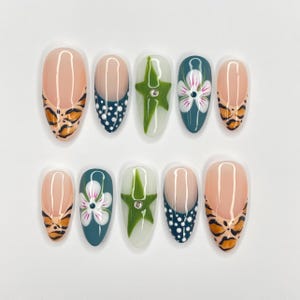 May include: Set of ten false nails with a variety of designs.  The nails feature a teal base with white polka dots, a white base with a green star, a teal base with a white flower, and a nude base with a tiger print.