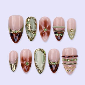 May include: A set of ten almond-shaped press-on nails featuring a mix of designs including tortoise shell patterns, sage green accents, metallic gold bands, and small green rhinestones. The nails have a glossy finish with varied decorative elements.