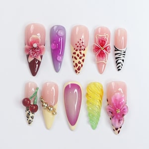 May include: Ten different nail designs featuring 3D flowers, cherries, and other decorative elements. The nails are painted in various colors, including pink, purple, red, and yellow.