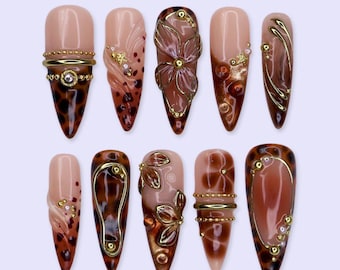 Unhas postiças artesanais com estampa de leopardo marrom outonal, formato amendoado longo com flores 3D e detalhes em dourado cromado.