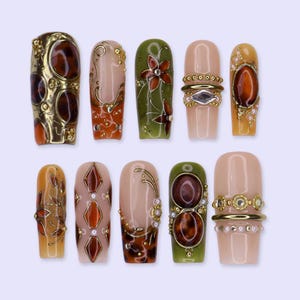 May include: A set of ten press-on nails featuring a variety of designs including gold metallic accents, brown tortoiseshell patterns, olive green backgrounds, and nude bases. The nails are decorated with small pearls, rhinestones, and intricate gold filigree lines.