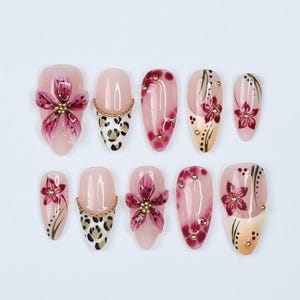 May include: Set of ten false nails with various designs. Some nails feature pink flowers, others have leopard print, and some have gold accents.
