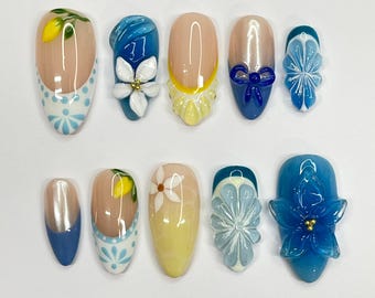 Puede incluir: Diez uñas artificiales ovaladas con varios diseños. Los diseños incluyen lunares azules y blancos, flores amarillas y blancas, flores azules y lazos azules.