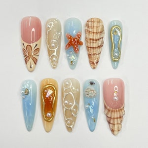 Uñas postizas largas almendradas con diseño de concha marina 3D y estrella de mar, ideales para el verano. Diseño único para vacaciones y eventos veraniegos.