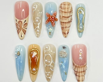 Uñas postizas largas almendradas con diseño de concha marina 3D y estrella de mar, ideales para el verano. Diseño único para vacaciones y eventos veraniegos.