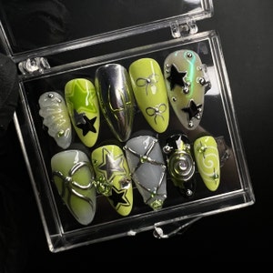 May include: Close-up of ten manicured fingernails with green and black nail art designs. The designs include stars, bows, and swirls.