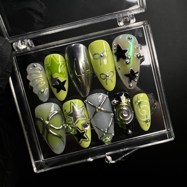 May include: Close-up of ten manicured fingernails with green and black nail art designs. The designs include stars, bows, and swirls.