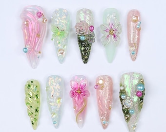 May include: Ten long, pointed, artificial nails with various designs. The designs include flowers, swirls, glitter, and iridescent finishes. Some nails have small pearl-like beads.