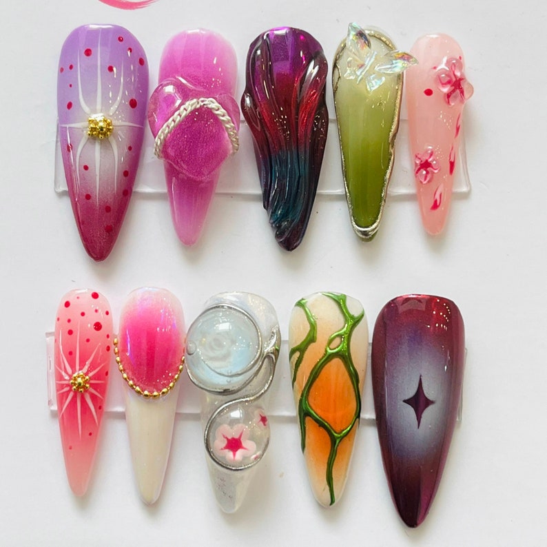 May include: Close-up of ten different nail designs. The designs include a pink and white floral design, a pink and white swirl design, a green and orange design, a purple and blue design, a green and white design, a pink and white design, a white and blue design, a red and white design, a pink and white design, and a pink and white design.