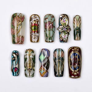 Puede incluir: Diez puntas de uñas decorativas con diseños intrincados en oro, verde, azul, rojo y blanco. Los diseños incluyen flores, mariposas y patrones geométricos.