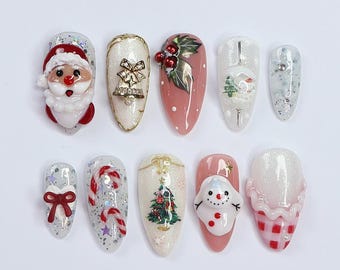 Könnte beinhalten: Zehn weiße und rosafarbene Weihnachtsmotive für die Nagelkunst. Die Designs beinhalten den Weihnachtsmann, eine Glocke, Stechpalme, einen Weihnachtsbaum, einen Zuckerstock, einen Schneemann und eine karierte Schleife.