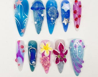 May include: A collection of ten long, pointed acrylic nails with various designs. The nails feature a range of colors, including blue, pink, and white, with embellishments like stars, flowers, and 3D elements. The designs include jellyfish, floral patterns, and abstract art.
