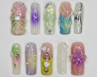 May include: Ten different nail designs featuring various colors, patterns, and embellishments. The designs include flowers, swirls, and abstract patterns. Some nails have pearls and other decorative elements.