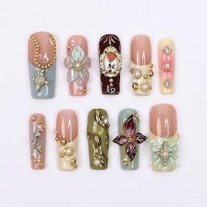 Puede incluir: Diez uñas artificiales con diferentes diseños. Las uñas están decoradas con perlas, pedrería, flores y una cadena. Las uñas son de varios colores, incluyendo azul, verde, rosa y blanco.