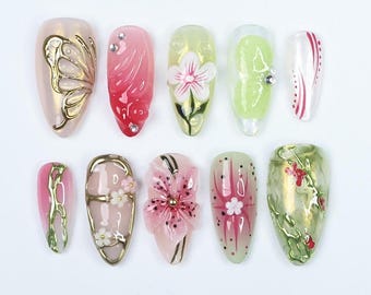 May include: Ten different nail designs featuring floral, butterfly, and geometric patterns. The designs are painted on almond-shaped nails and feature a variety of colors, including pink, green, white, and gold.
