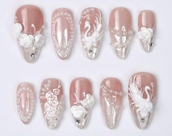 May include: Set of ten false nails with a pink base and white 3D floral and swan designs. The nails are decorated with pearl beads and rhinestones.