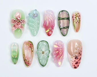 May include: A set of 10 decorative nail tips with various designs, including flowers, butterflies, and abstract patterns. The tips are in shades of green, pink, and white.