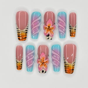 May include: Set of ten false nails with a pink and blue ombre design. Some nails feature a 3D flower design with a tiger stripe accent.