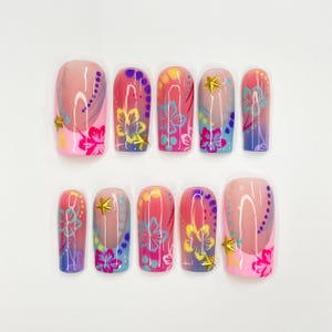 May include: Set of ten false nails with a pink, blue, and yellow ombre design. Each nail features a floral pattern and a gold star accent.