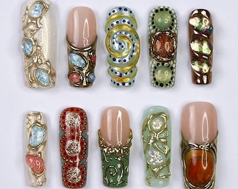 May include: Ten different nail designs featuring intricate details, including gold accents, gems, and swirls. The designs are on a white background.