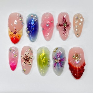 May include: Ten colorful nail art designs featuring flowers, swirls, and rhinestones. The designs are painted on oval-shaped fake nails.