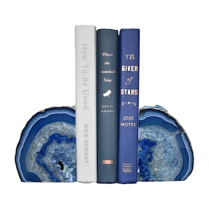 May include: Blue agate bookends with three books on top. The book titles are "How To Be Good" by Nick Hornby, "Where the Crawdads Sing" by Delia Owens, and "The Giver of Stars" by Jojo Moyes.