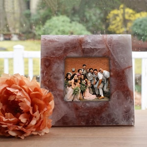 May include: A pink and white crystal picture frame with a group of people smiling in a photo inside. The frame is made of natural stone and has a rustic look.