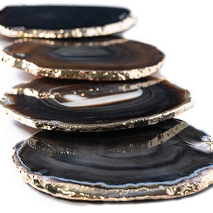 May include: Set of four agate coasters with gold trim. Each coaster features a unique natural pattern of black, brown, and white agate.