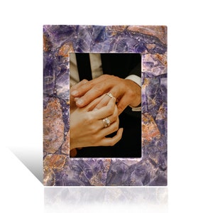 May include: A purple amethyst picture frame with a photo of a couple's hands with wedding rings.
